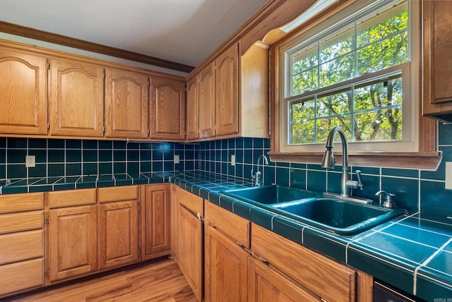 kitchen featuring tasteful backsplash, sink, light hardwood / wood-style floors, ornamental molding, and tile countertops