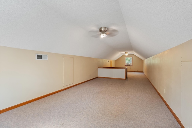 additional living space with ceiling fan, vaulted ceiling, a textured ceiling, and light carpet