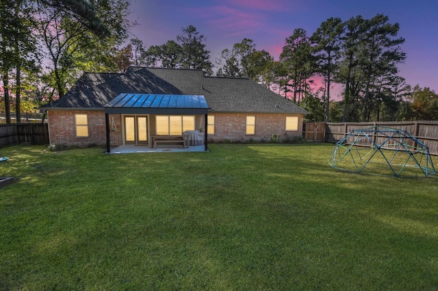 back house at dusk featuring a yard and a patio