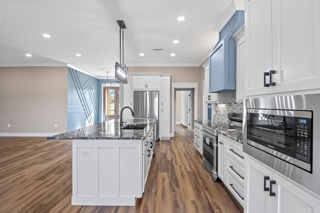 kitchen featuring dark stone countertops, sink, white cabinetry, appliances with stainless steel finishes, and a center island with sink