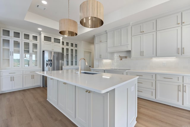 kitchen featuring backsplash, white cabinets, a center island with sink, and sink