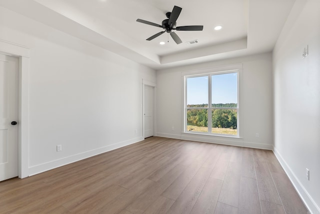 unfurnished room featuring light wood-type flooring, ceiling fan, and a tray ceiling