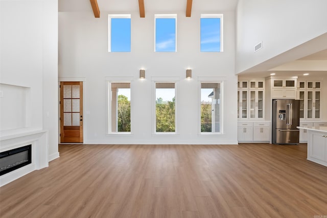 unfurnished living room featuring high vaulted ceiling, beam ceiling, and light hardwood / wood-style flooring