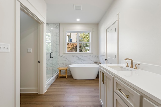 bathroom with hardwood / wood-style floors, shower with separate bathtub, vanity, and tile walls