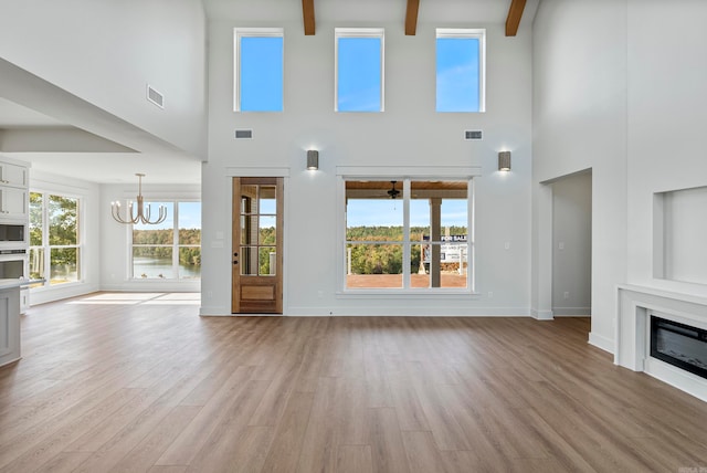 unfurnished living room with light hardwood / wood-style flooring, beam ceiling, high vaulted ceiling, and a wealth of natural light