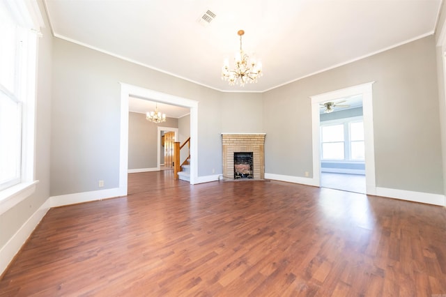 unfurnished living room with ceiling fan with notable chandelier, a brick fireplace, dark hardwood / wood-style floors, and ornamental molding