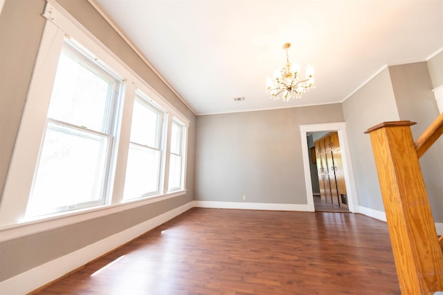 empty room featuring dark wood-type flooring, ornamental molding, and a notable chandelier