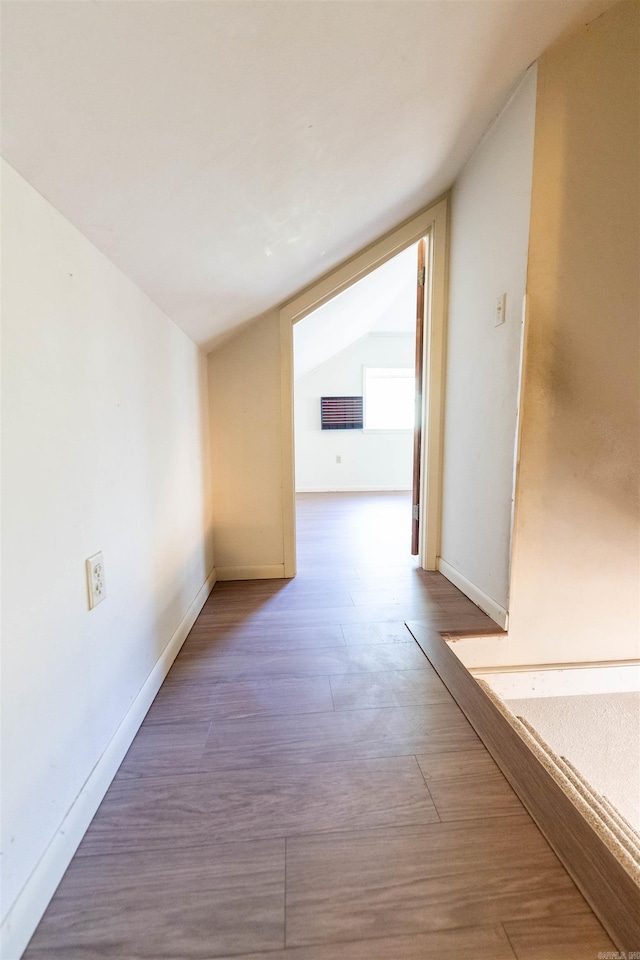 corridor with hardwood / wood-style floors and vaulted ceiling