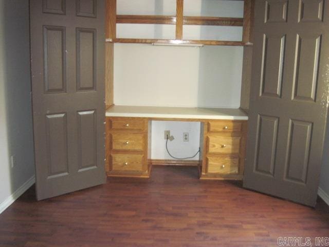 unfurnished office featuring dark hardwood / wood-style floors and built in desk