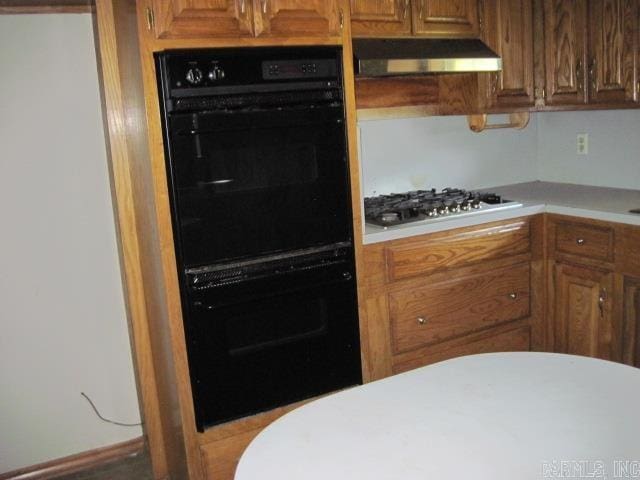 kitchen featuring black double oven, stainless steel gas stovetop, and range hood