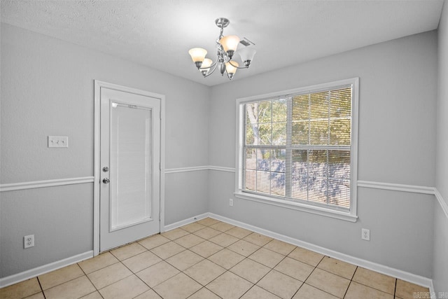 tiled empty room featuring a chandelier and a textured ceiling