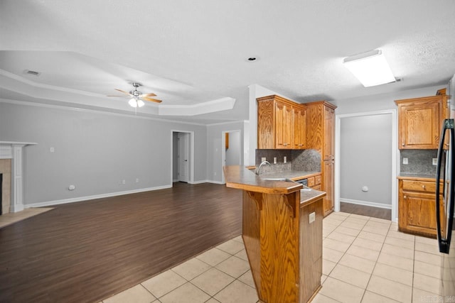 kitchen featuring kitchen peninsula, tasteful backsplash, light hardwood / wood-style flooring, a kitchen breakfast bar, and a tray ceiling