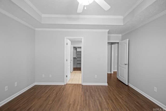 unfurnished bedroom with ceiling fan, crown molding, a spacious closet, a closet, and dark hardwood / wood-style floors