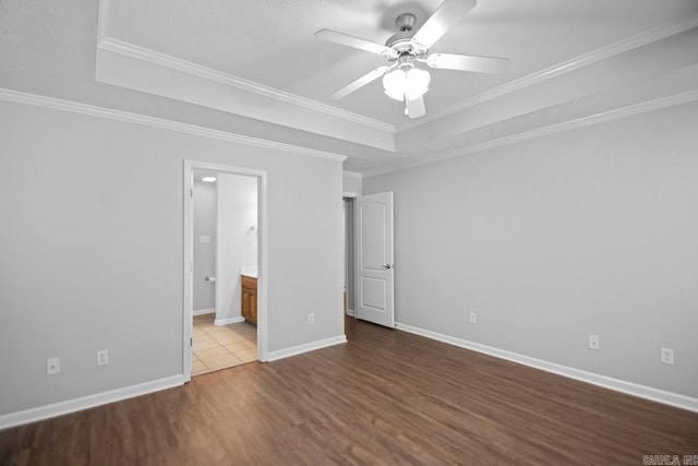 unfurnished bedroom featuring ceiling fan, connected bathroom, ornamental molding, a tray ceiling, and hardwood / wood-style floors