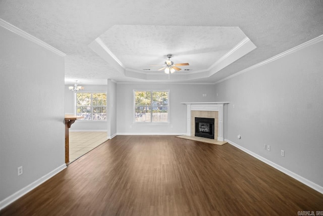 unfurnished living room with a textured ceiling, a tray ceiling, ceiling fan with notable chandelier, crown molding, and dark hardwood / wood-style flooring