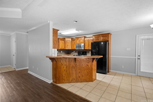 kitchen featuring ornamental molding, kitchen peninsula, tasteful backsplash, black appliances, and a breakfast bar