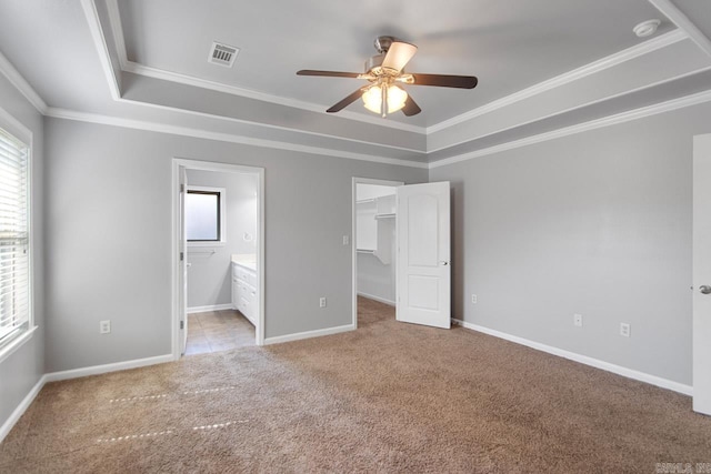 unfurnished bedroom with ceiling fan, a raised ceiling, connected bathroom, a walk in closet, and light colored carpet