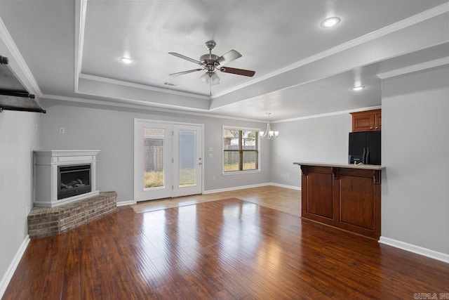 unfurnished living room with ceiling fan with notable chandelier, a fireplace, ornamental molding, and dark hardwood / wood-style floors