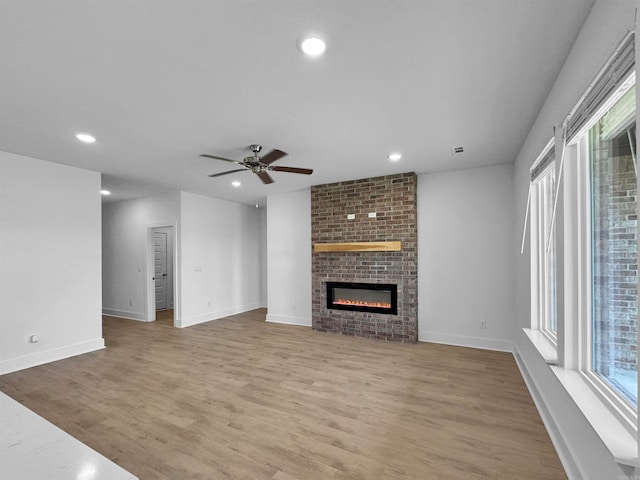 unfurnished living room featuring a brick fireplace, ceiling fan, and light hardwood / wood-style flooring