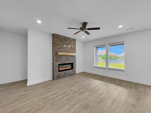 unfurnished living room featuring ceiling fan, a brick fireplace, and light hardwood / wood-style floors