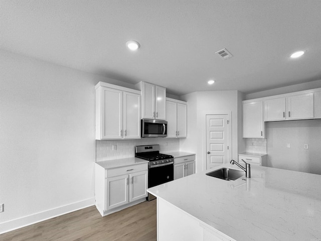 kitchen featuring sink, appliances with stainless steel finishes, wood-type flooring, white cabinets, and decorative backsplash