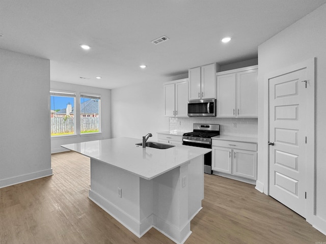 kitchen with light wood-type flooring, stainless steel appliances, white cabinets, and a center island with sink