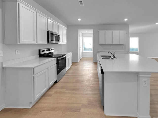 kitchen with appliances with stainless steel finishes, white cabinetry, a center island with sink, and light wood-type flooring