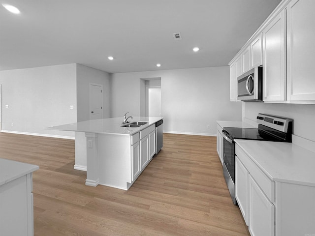 kitchen featuring white cabinetry, stainless steel appliances, light wood-type flooring, and a center island with sink