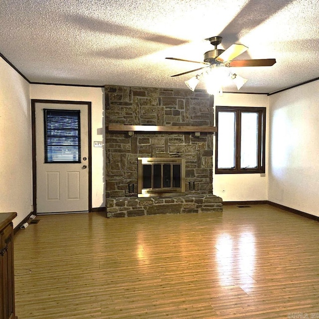 unfurnished living room with ceiling fan, a stone fireplace, a textured ceiling, dark wood-type flooring, and crown molding