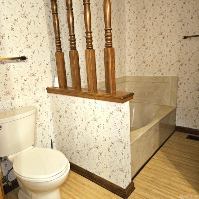 bathroom with a washtub, hardwood / wood-style floors, and toilet