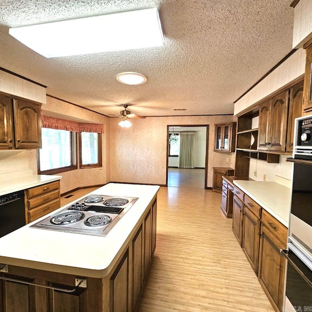 kitchen featuring light wood-type flooring, a kitchen island, ceiling fan, appliances with stainless steel finishes, and a textured ceiling