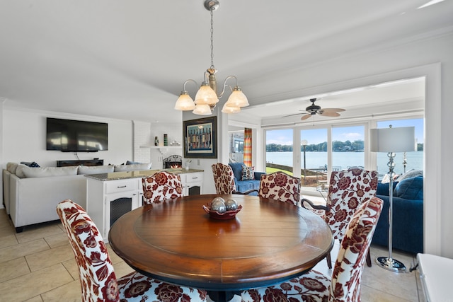 tiled dining space featuring a water view, a brick fireplace, ceiling fan with notable chandelier, and crown molding