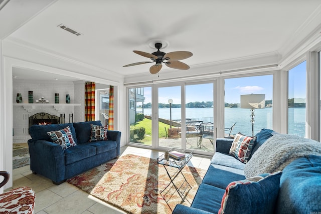 tiled living room featuring ornamental molding, a water view, a brick fireplace, and ceiling fan