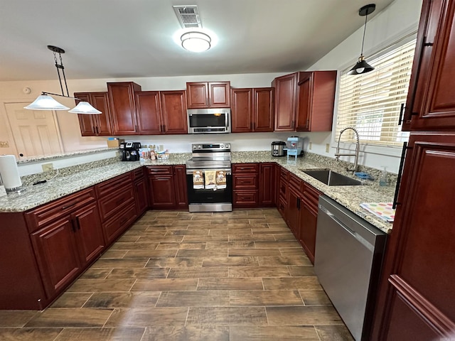 kitchen with light stone countertops, hanging light fixtures, appliances with stainless steel finishes, and sink