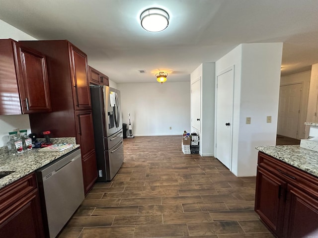 kitchen with dark wood-type flooring, appliances with stainless steel finishes, and light stone counters