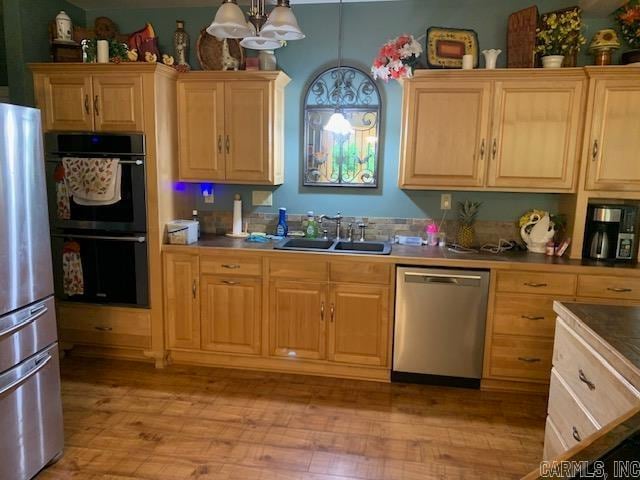 kitchen with an inviting chandelier, sink, hanging light fixtures, light wood-type flooring, and stainless steel appliances