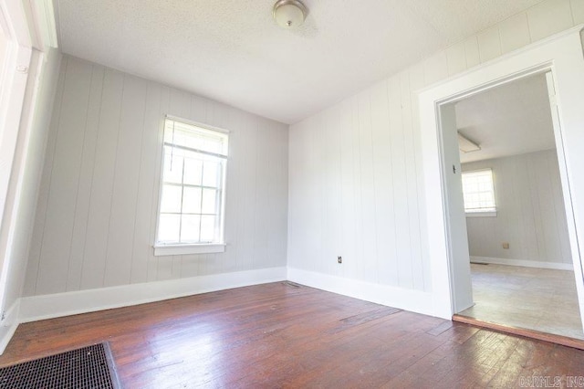 empty room with dark hardwood / wood-style floors, wooden walls, and a textured ceiling