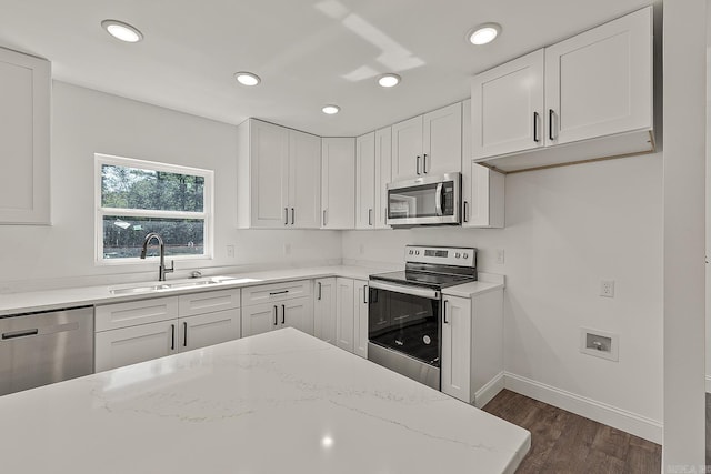 kitchen with light stone countertops, dark hardwood / wood-style floors, sink, white cabinetry, and appliances with stainless steel finishes