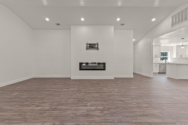 unfurnished living room featuring vaulted ceiling, sink, and light hardwood / wood-style floors