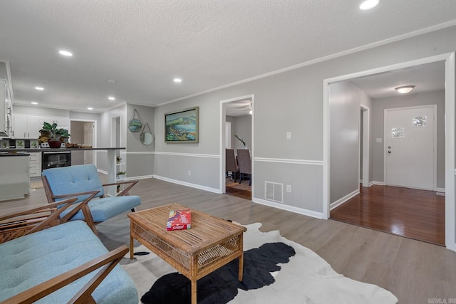 living room with wine cooler, crown molding, hardwood / wood-style floors, and a textured ceiling