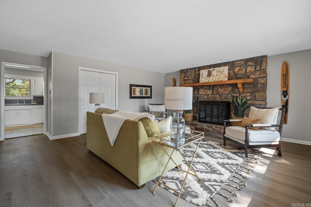 living room featuring sink, dark hardwood / wood-style flooring, a textured ceiling, and a stone fireplace