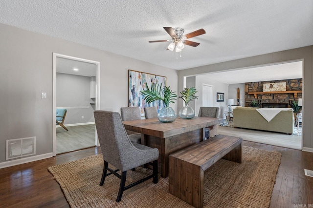 dining room featuring ceiling fan, a textured ceiling, a fireplace, and dark hardwood / wood-style floors