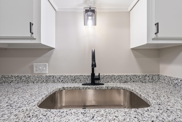 interior details with light stone countertops, crown molding, sink, and white cabinets