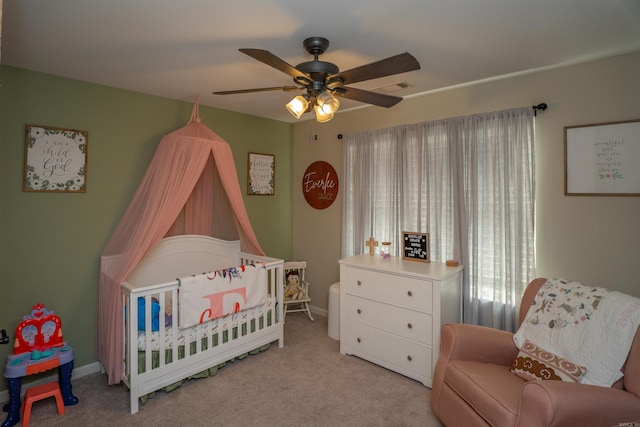 carpeted bedroom featuring a crib and ceiling fan