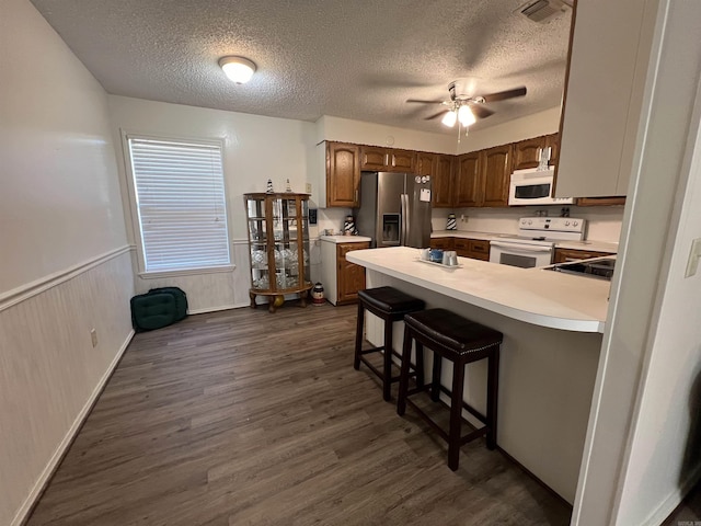 kitchen with a breakfast bar, white appliances, dark hardwood / wood-style floors, and a textured ceiling