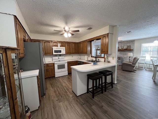 kitchen featuring sink, kitchen peninsula, white appliances, dark wood-type flooring, and a breakfast bar area