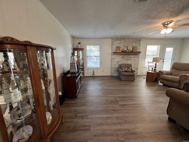 living room with a brick fireplace, a textured ceiling, dark hardwood / wood-style floors, and plenty of natural light