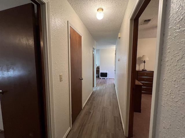 hallway with heating unit, hardwood / wood-style floors, and a textured ceiling