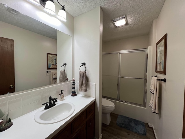 full bathroom featuring enclosed tub / shower combo, vanity, wood-type flooring, a textured ceiling, and toilet