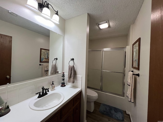 full bathroom featuring toilet, wood-type flooring, shower / bath combination with glass door, vanity, and a textured ceiling